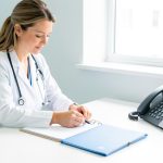 Continuité d’activité d’un cabinet médical : préparer les absences imprévues Médecin généraliste organisant un bureau médical lumineux avec un agenda vierge, un dossier patient fermé et un téléphone.