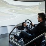 Un homme concentré conduit un simulateur automobile dynamique dans un espace moderne à Landerneau, avec un écran affichant un circuit.