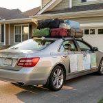 Check-list long trajet en voiture : préparer son départ sans oubli Voiture familiale chargée de bagages et de cartes routières posées devant une maison, prête pour un long voyage.